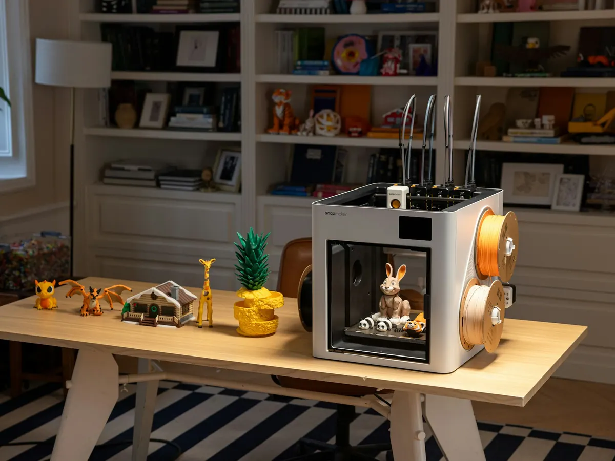 A small 3D printer on a wooden desk at home, next to a row of colourful printed figures